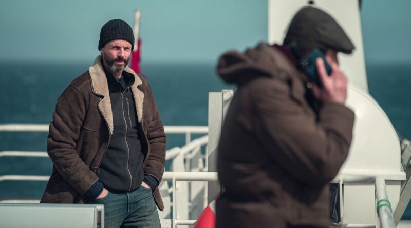 Detective Carl Morck stands on a ferry deck, watching as a man speaks on the phone in Netflix’s Department Q.