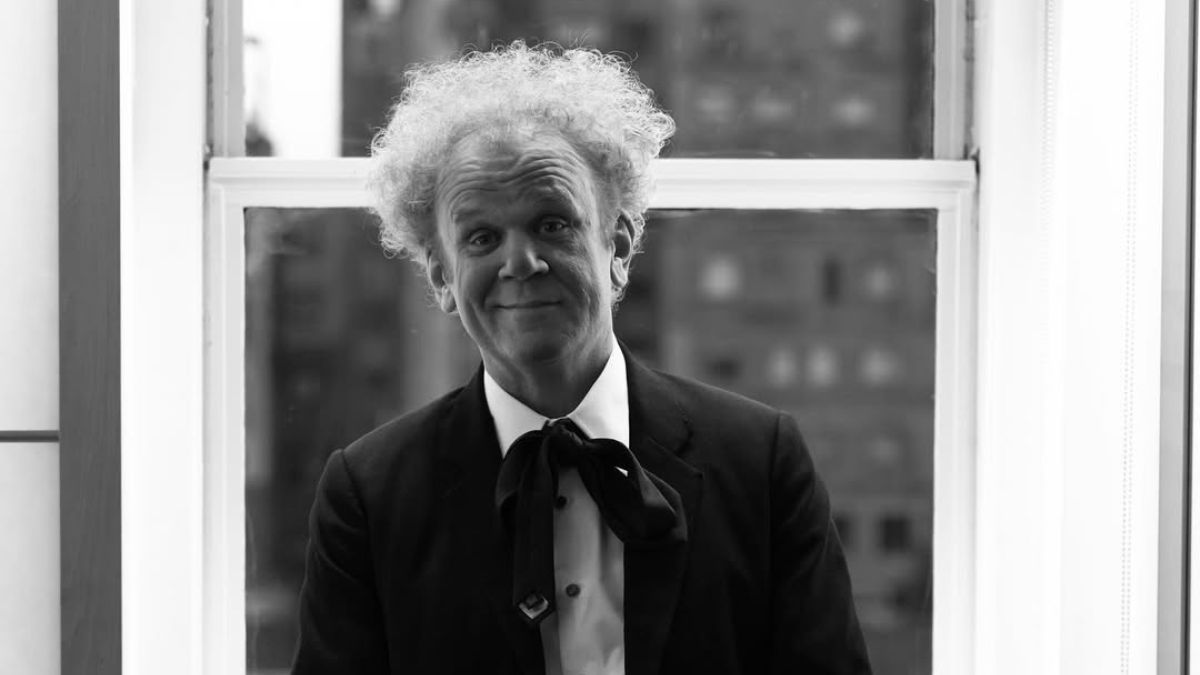 John C. Reilly in black suit with bowtie posing near a window during Mr. Romantic press tour