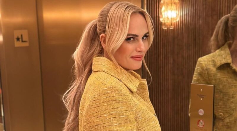 Rebel Wilson smiling in a yellow outfit in a luxury elevator lobby
