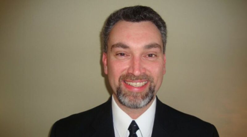 Headshot of a man in a suit with a goatee and smile, against a neutral background
