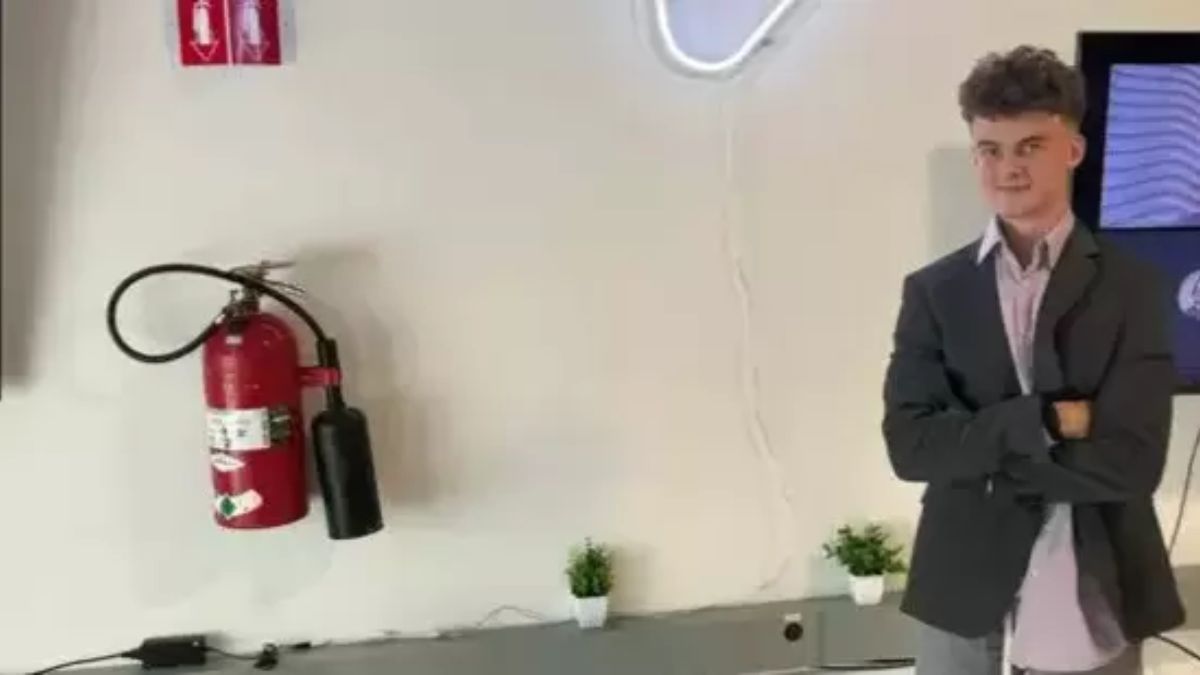 Edward Coristine, known as "Big Balls," stands in a tech-style office beside a fire extinguisher, arms folded.