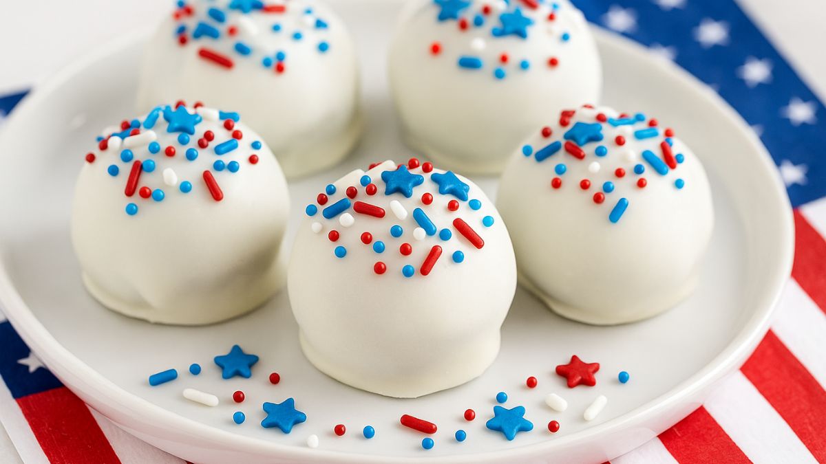 No-bake Oreo truffles coated in white chocolate and topped with red, white, and blue sprinkles, served on a round plate over a patriotic napkin.