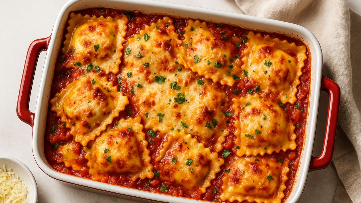 A high-resolution photograph showcases a baked ravioli lasagna in a white ceramic dish with red handles, featuring golden cheese, marinara sauce, and chopped parsley.