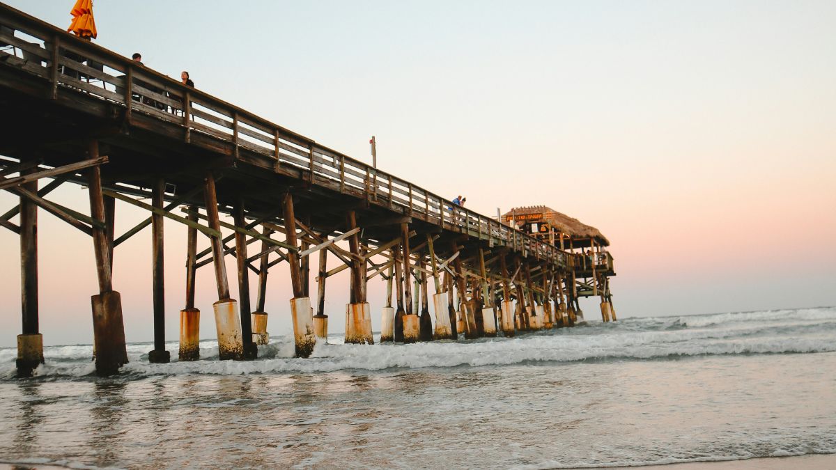 Wooden pier at Cocoa Beach, Florida at sunset with reflections on wet sand