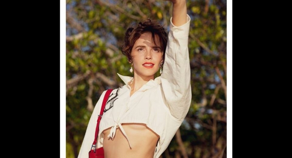 Emma Watson posing outdoors in a cropped white shirt with a red shoulder bag