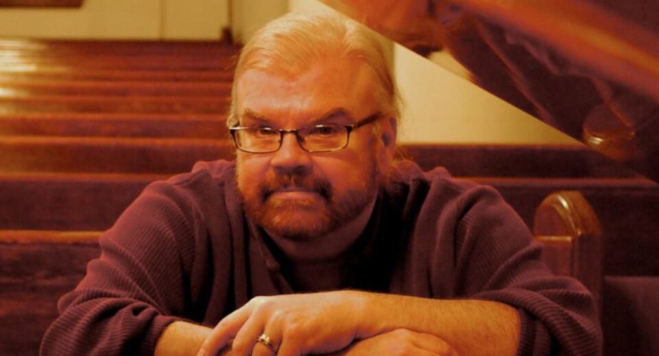 James Carter Cathcart sitting quietly in a church pew, wearing glasses and a purple sweater