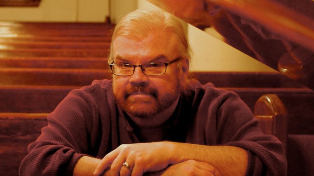 James Carter Cathcart sitting quietly in a church pew, wearing glasses and a purple sweater