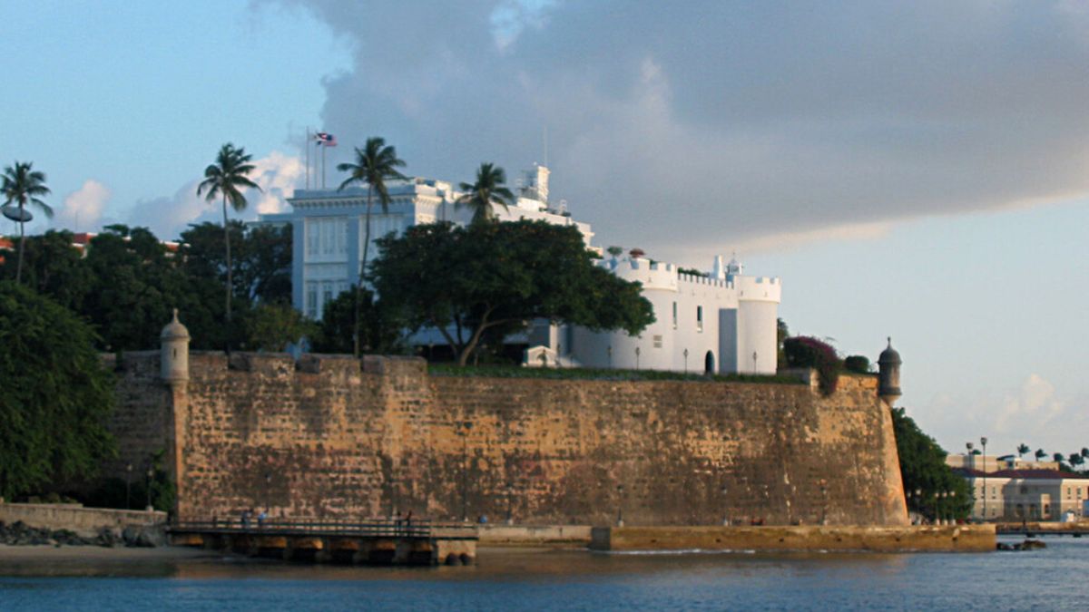 View of La Fortaleza atop a historic stone fort wall in San Juan, Puerto Rico, with palm trees and coastal waters