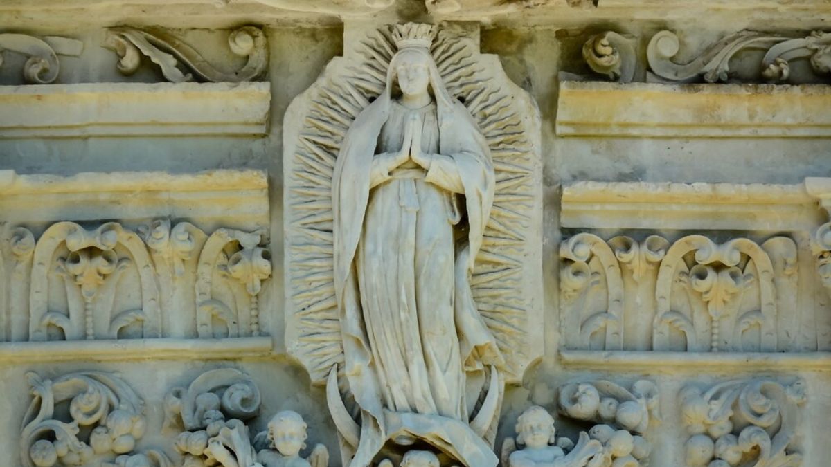 Detailed stone carving of Our Lady of Guadalupe surrounded by angels on the facade of Mission San José in San Antonio