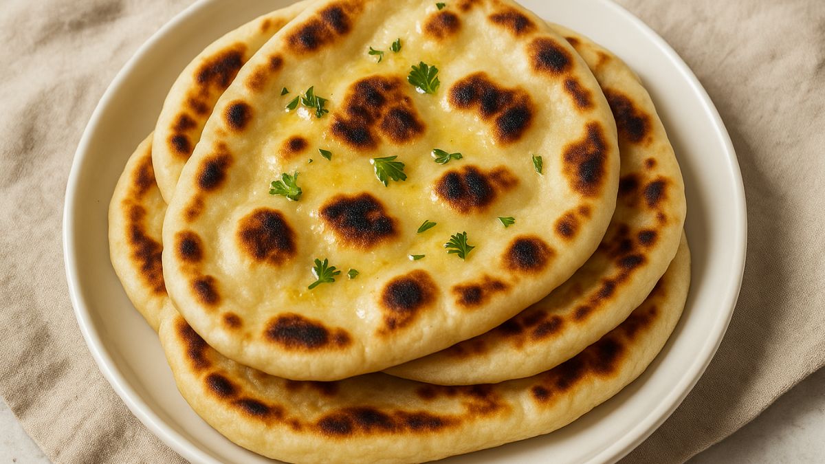 Fresh homemade naan bread stacked on a plate with garlic butter